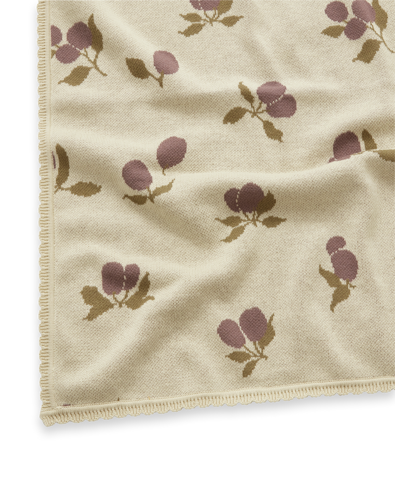 Jacquard-Strickdecke in weicher Baumwollqualität mit dekorativem Jakobsmuschel-Wellenrand. Hergestellt aus 100% OEKO-TEX® 100 zertifizierter Baumwolle. Das charakteristische Muster Prune Beige, aus zarten Pflaumen auf hellem beigefarbenem Jacquard-Strick ist ein absolutes Must-Have dieser wunderschönen Kollektion.