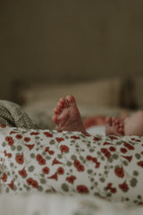 Baby liegt in Decke eingewickelt. Jersey-Decke in weicher, gerippter Bio-Baumwollqualität mit Paspelierung am Rand. Die Decke ist doppellagig mit einem schönen handgezeichneten Druck auf der Vorderseite und einer einfarbigen Rückseite.

