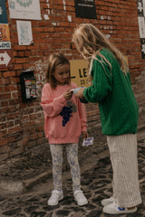 Mädchen trägt oversized-Sweatshirt aus weicher Bio-Baumwolle mit handgezeichnetem Print, Rundhalsausschnitt, überschnittenen Schultern & Rippbündchen an Ärmeln und Saum.