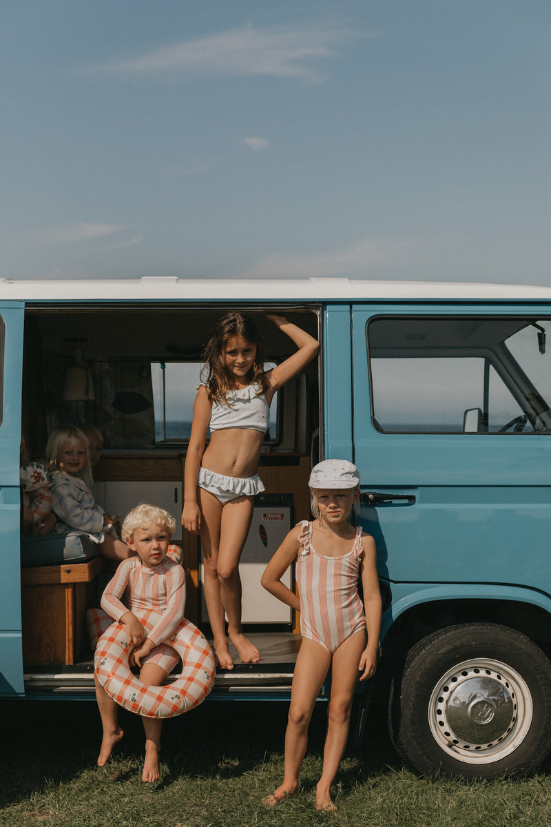 Kinder in Bademode. Bikini, Badeanzug, Badeoverall, Shorts. Vollständig gefütterte klassische Bademode mit dekorativen Rüschendetails, hergestellt aus recyceltem, weichem und dehnbarem Strukturgewebe. Farbe apricot/beige, UV Badeanzug. 