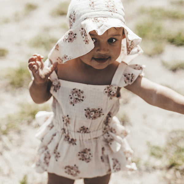 Kind trägt Body Bebe im zarten Frühlings-Mohnblumen-Print mit elastischem Gummizug in der Taille und an den Beinen für eine bequeme Passform.