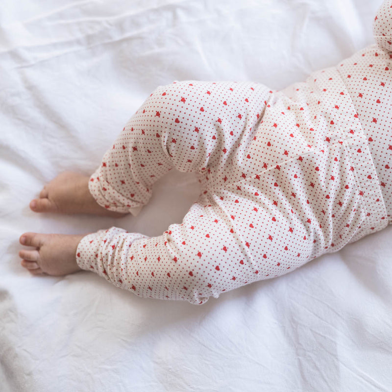 Baby trägt komfortable weiche Leggings für Babies und Kleinkinder, aus weicher Bio-Baumwoll im zarten Print aus roten kleinen Herzen. 