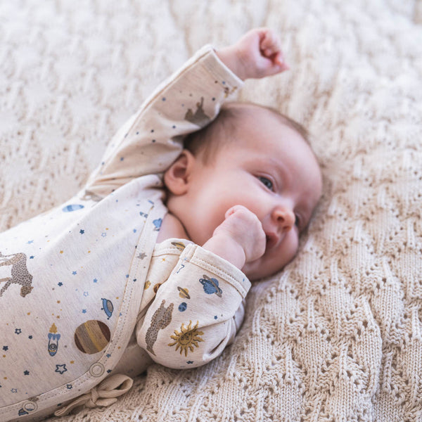 Baby im himmlisch weichen Wickelbody mit seitlichen Druckknöpfen und Schleife zum Binden im neuen Leo Espace Muster aus Bio-Baumwolle und Modal. 