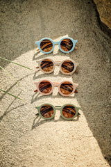 Diverse Sonnenbrillen liegen im Sand am Strand. Perfekt für deine Sommer-Outfit. 