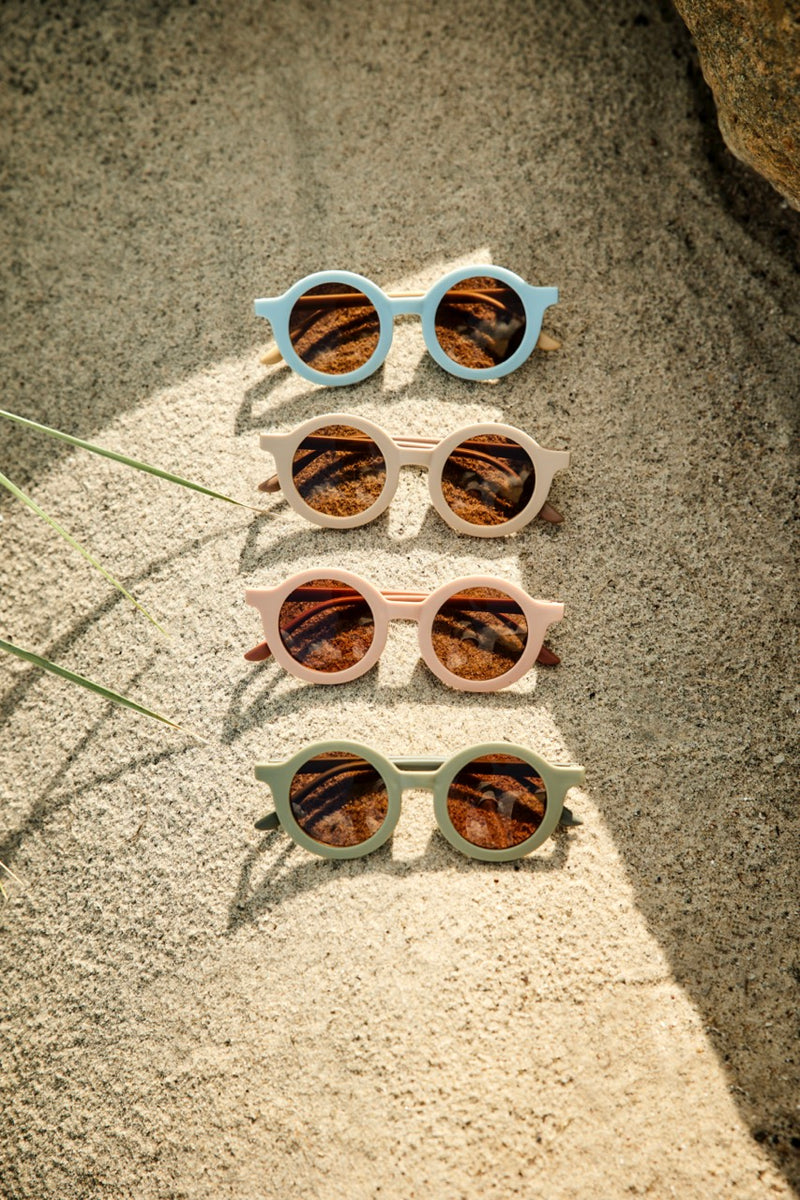 Diverse Sonnenbrillen liegen im Sand am Strand. Perfekt für deine Sommer-Outfit. 