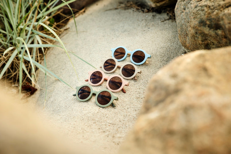 Diverse Sonnenbrillen liegen im Sand am Strand. Perfekt für deine Sommer-Outfit. 
