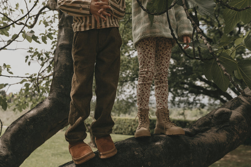 Kinder tragen Leggings und Cordhosen.  Leggings mit schönem handgezeichnetem Aufdruck aus weichem Bio-Ripp-Jersey mit glatter Innenseite und weichem Gummibund, mit zarten roten Blumen und Klee auf hellem Hintergrund. 