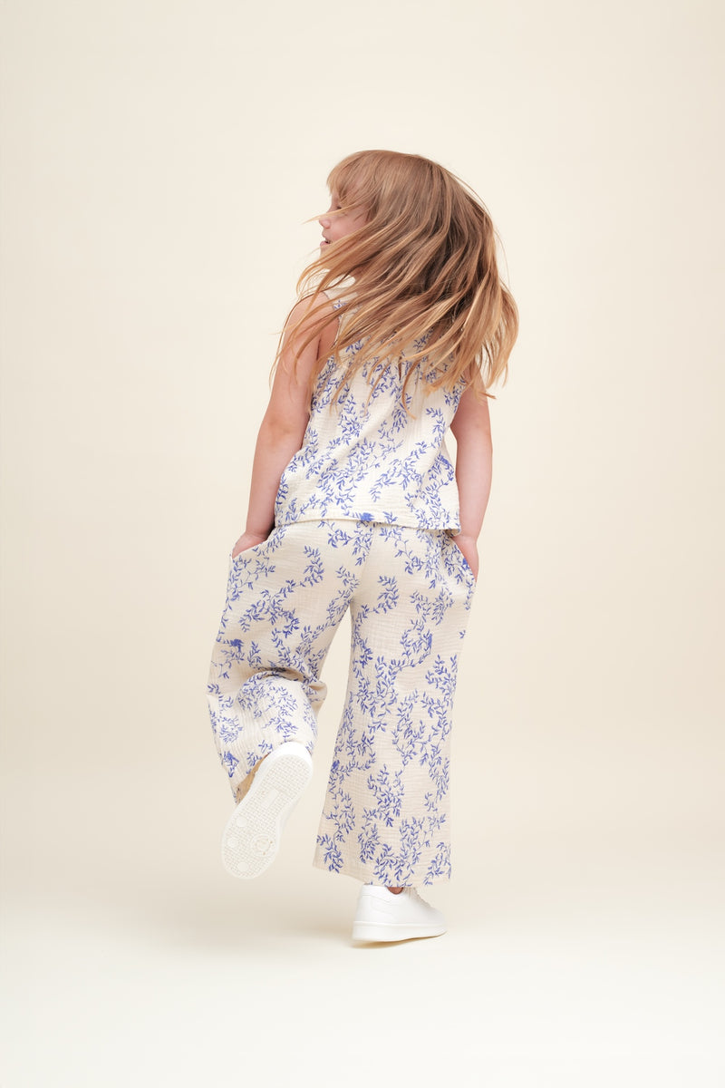 Mädchen trägt Culottes aus weichem Baumwoll-Musselin in Beige mit gepolstertem, verstellbarem Gummizug, dekorativer Rüsche und Seitentaschen – unisex und knöchellang - Rückansicht der Hose. 