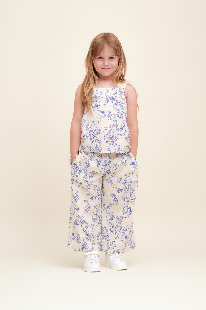 Mädchen trägt Culottes aus weichem Baumwoll-Musselin in Beige mit gepolstertem, verstellbarem Gummizug, dekorativer Rüsche und Seitentaschen – unisex und knöchellang.