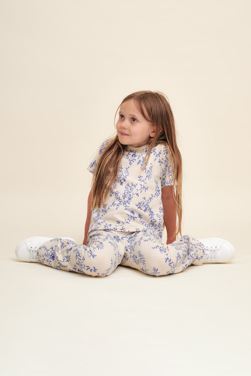 Flared Kinderleggings aus Bio-Baumwolle mit ausgestelltem Bein, handgezeichnetem Print und weichem, elastischem Bund – Mädchen trägt Leggings zur gleichen Bluse sitzend auf dem Boden.