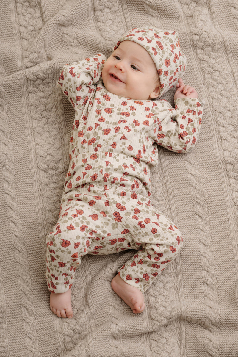 Baby liegend in Leggings und Langarmbody.  Leggings mit schönem handgezeichnetem Aufdruck aus weichem Bio-Ripp-Jersey mit glatter Innenseite und weichem Gummibund, mit zarten roten Blumen und Klee auf hellem Hintergrund. 